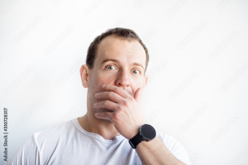 Closeup portrait of surprised 30 years old caucasian white man on white background in white t-shirt. Front view of shocked muscular man covering mouth with hand isolated on white. Scared expression Closeup portrait of surprised 30 years old caucasian white man on white background in white t-shirt. Front view of shocked muscular man covering mouth with hand isolated on white. Scared expression