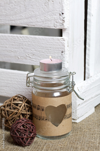 Glass jar wrapped by paper with notes. Heart cut out in paper. It is on a linen cloth. Near ratang balls and a wooden box of boards. photo