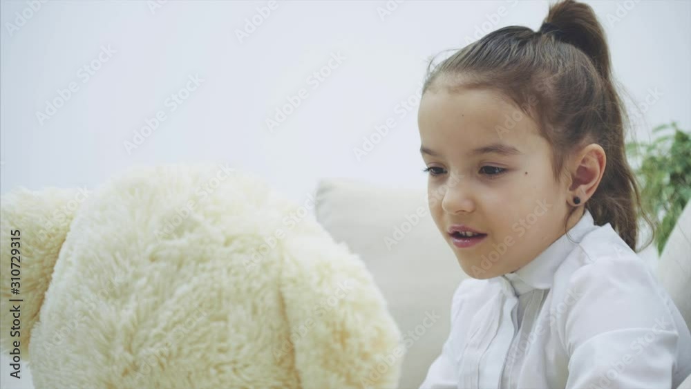 Adorable little girl sitting on the sofa, talking with her teddy. Adorable little girl sitting on the sofa, talking with her teddy.