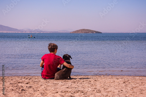 Young woman sitting on the seashore with a black dog