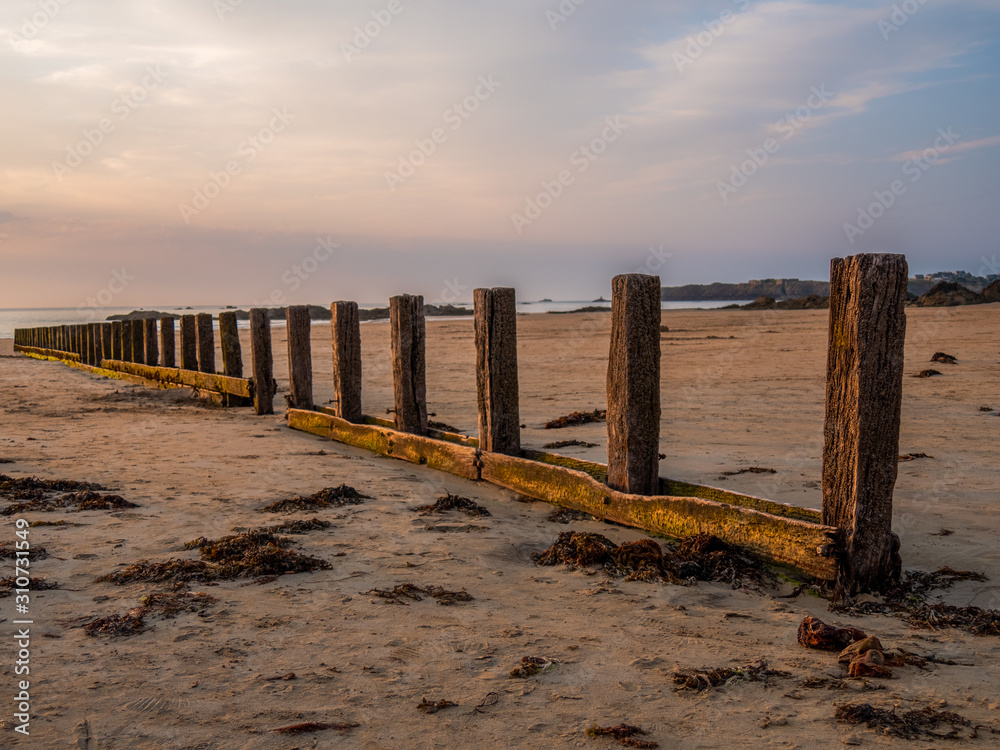 A wooden breakwater on the sand beach at the beautiful sunset.