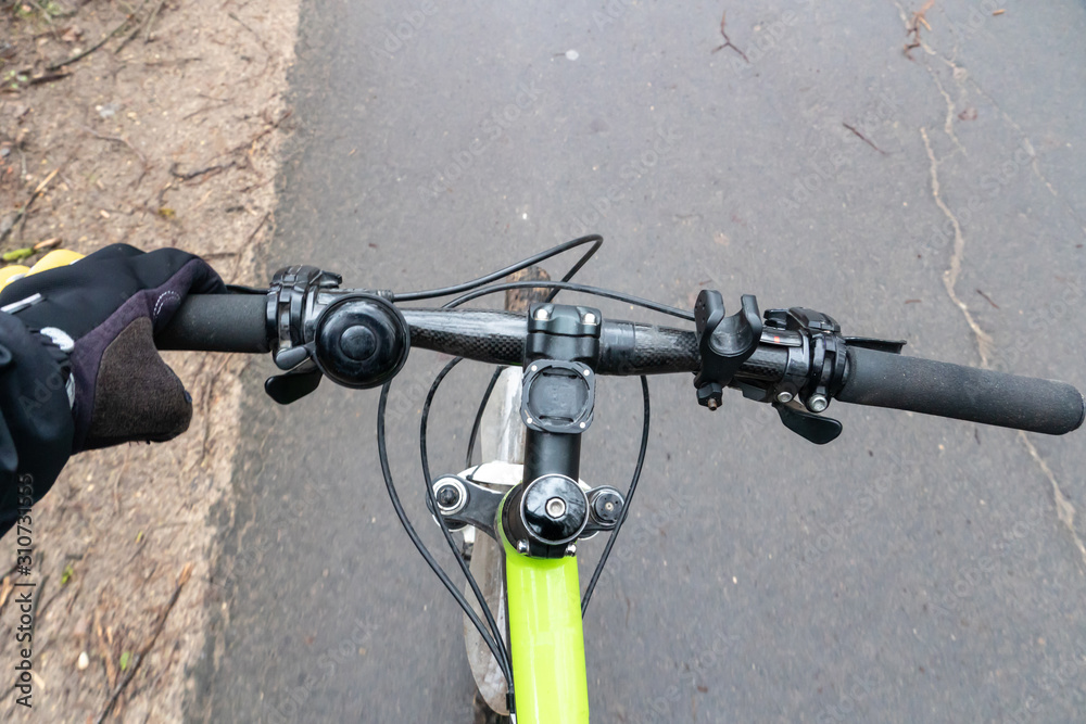 Cyclist on the bike path. First person view. Focus on the hand and the handlebars. It's cold, man in cycling clothes. On the track leaves and branches. Bike controls closeup.