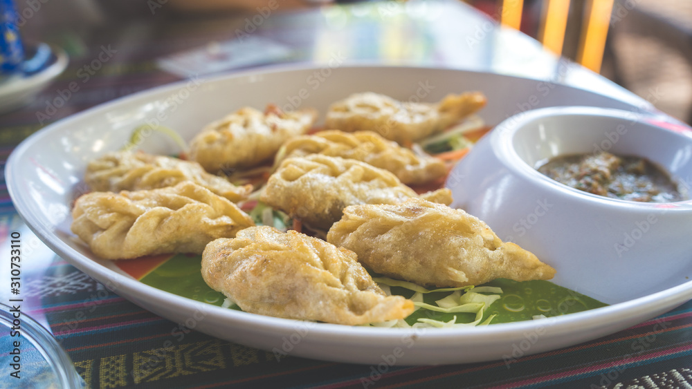 A dish of the tibetan fried momo with a sauce. Momo is a dish of dough with a filling. A dish of the tibetan fried momo with a sauce. Momo is a dish of dough with a filling.