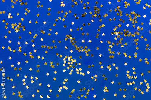Delicate golden glitter star confetti on blue background. Creative and moody color of the picture.