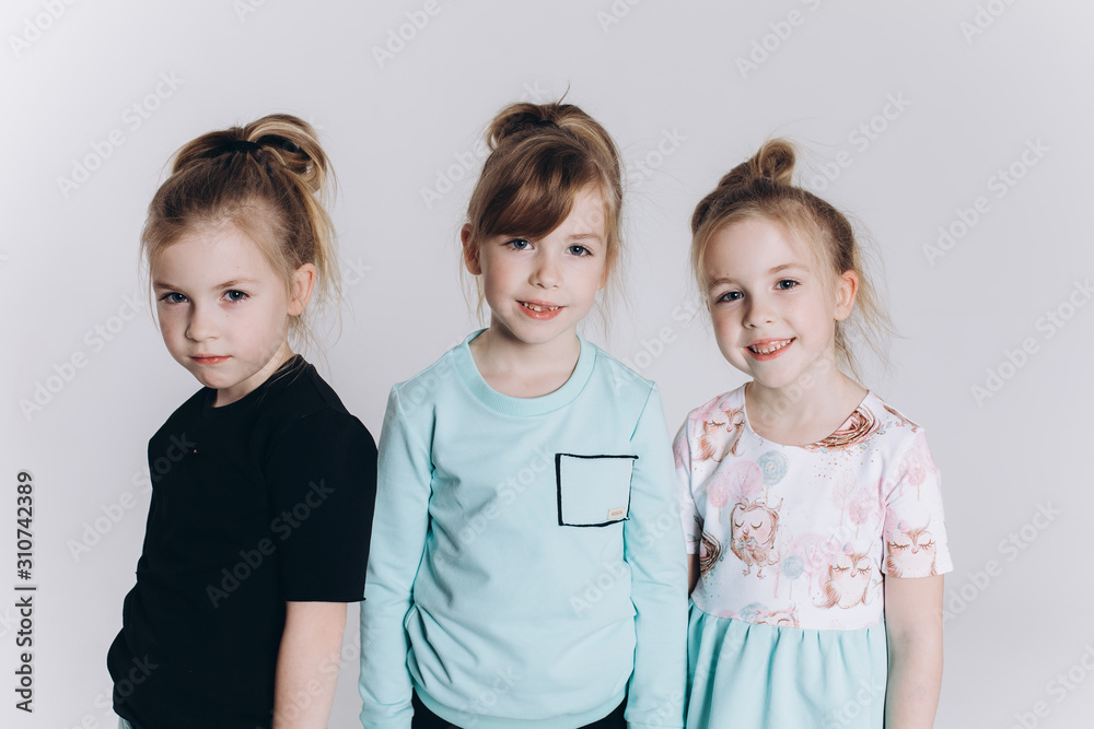 Happy cute adorable blondie triplets girls posing in studio together on isolated background. Childhood, children, twins concept. Smiling girls playing together Happy cute adorable blondie triplets girls posing in studio together on isolated background. Childhood, children, twins concept. Smiling girls playing together