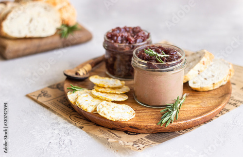 Fresh homemade chicken liver pate and onion chutney (marmalade) in a jar, bread and crackers on a wooden plate. Light grey background, selective focus.