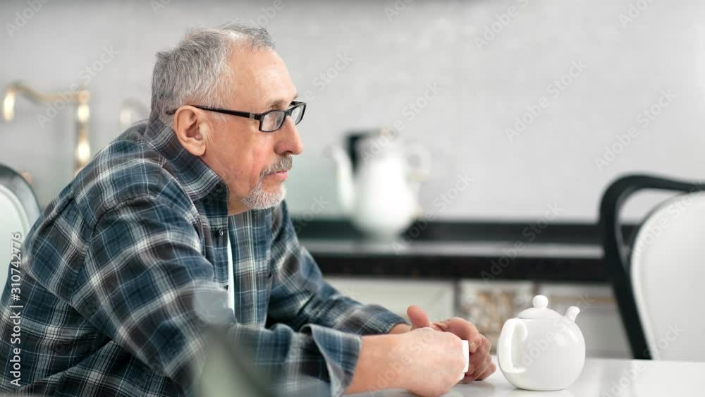Lonely pensive aging male drinking tea at white kitchen having calmness emotion medium close-up Lonely pensive aging male drinking tea at white kitchen having calmness emotion medium close-up