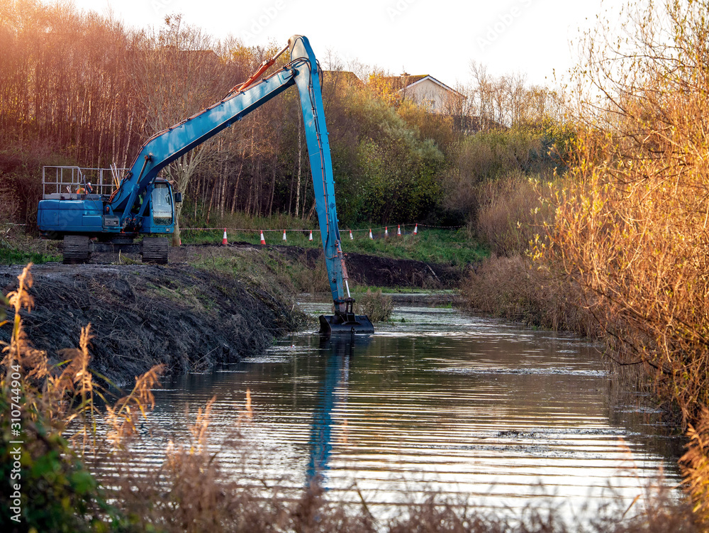Blue excavator cleaning river in a park, Warm morning light.