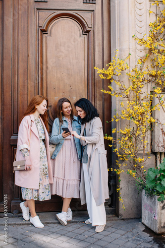 Wallpaper Mural Three stylish girlfriends searching information at phone while standing near old beautiful door in the street Torontodigital.ca