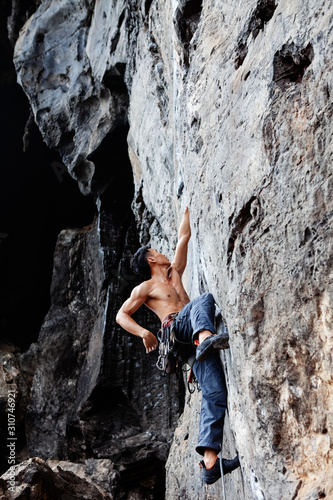 Muscular man climbing up on rocky wall