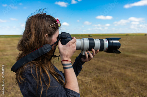 Close up, head shot of a young female photographer with long hair taking pictures outdoor with a long zoom lens in a rural environment