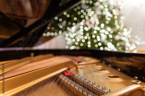 Golden piano interior with visible strings in the foreground. In the background a blurred Christmas tree decorated with ornaments and Christmas tree lights. Big bokeh and sectional focus. photo