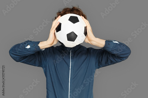 Fototapeta Naklejka Na Ścianę i Meble -  Sporty Lifestyle. Teenager boy standing isolated on grey covering face with soccer ball close-up