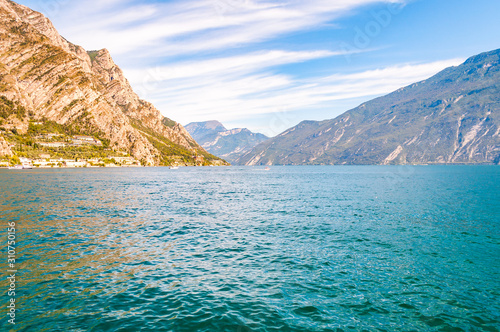 Amazing Garda lake in Lombardy, Italy surrounded by high dolomite mountains. Boats and yacht floating on the lake. Various hotels and private houses built on the rocky shores of the lake