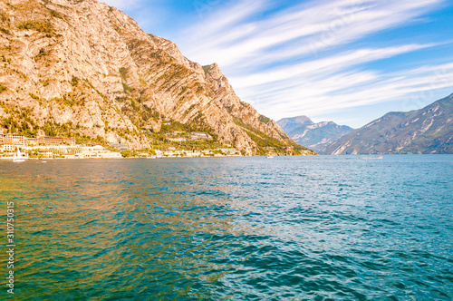 Amazing Garda lake in Lombardy, Italy surrounded by high dolomite mountains. Boats and yacht floating on the lake. Various hotels and private houses built on the rocky shores of the lake
