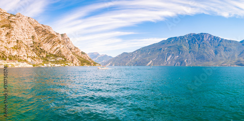 Panorama of amazing Garda lake in Lombardy, Italy surrounded by high dolomite mountains. Boats and yacht floating on the lake. Various hotels and private houses built on the rocky shores of the lake