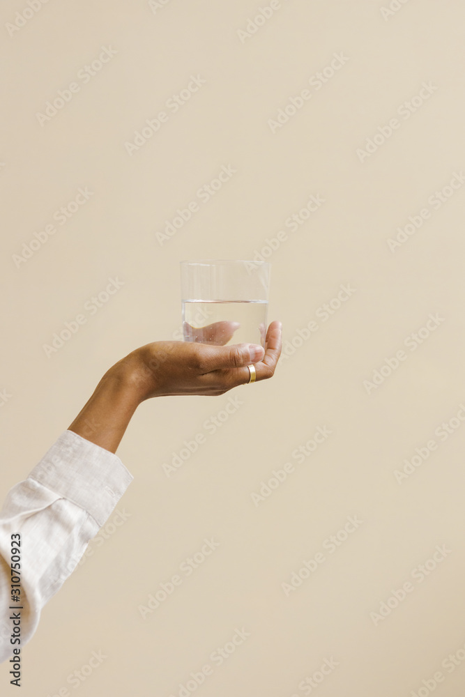 hand holding a water glass in front of tan background