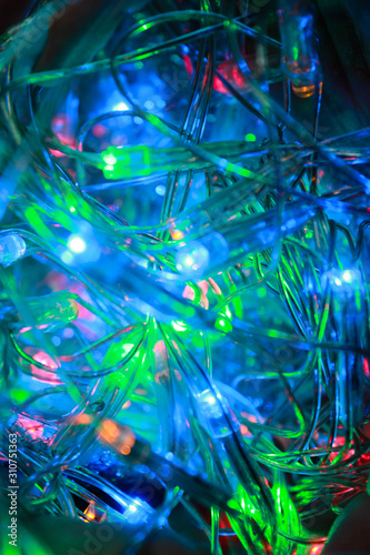 Blurred close-up photo of a multi-colored Christmas electric garland. Shining holiday lights of blue, green and red LED lamps with a transparent wire, bright color image.