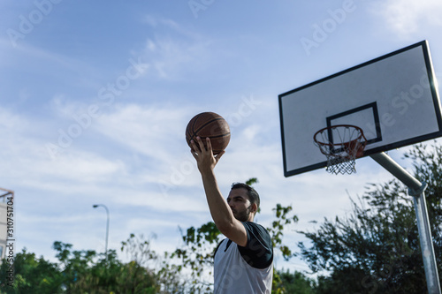 Basketball player throws the ball with his back to the basket of an outdoor court © Óscar