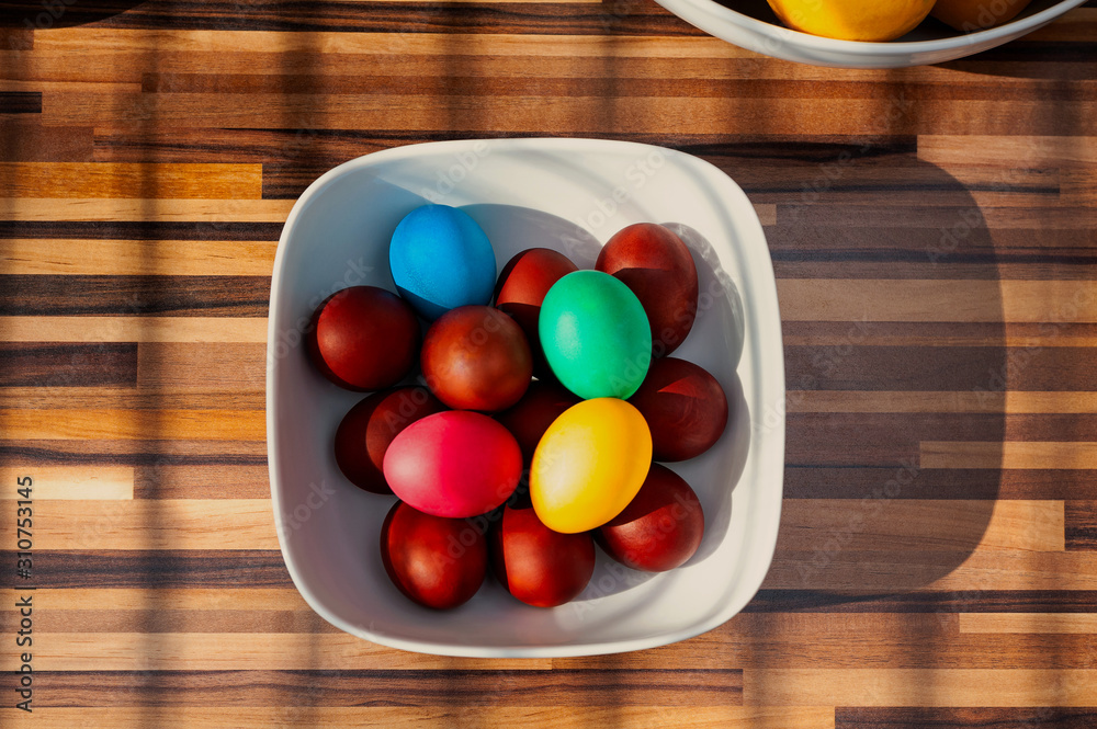 Multicolored Easter eggg in square white bowl on wooden kitchen worktop. Multicolored Easter eggg in square white bowl on wooden kitchen worktop.