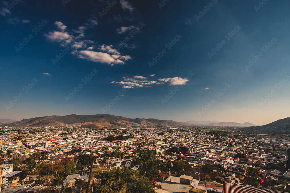 Panorama of Oaxaca, Mexico, on a sunny day with blue sky, looking from Benito Juarez statue above the city. Some white clouds are seen in the centre of the frame.