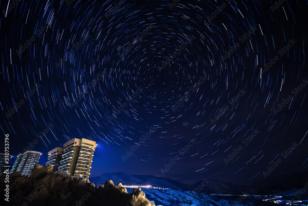 Fototapeta premium Star trail panorama over the apartment blocks in the ski village of Le Corbier, high in the French Alps around midnight. Star Polaris is seen in the center.