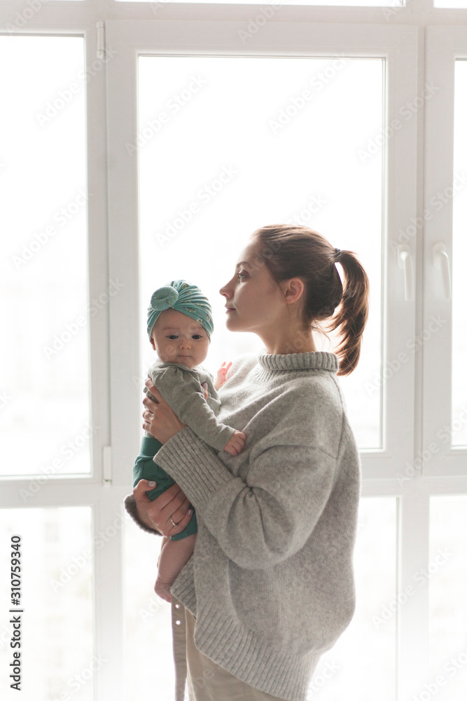 mother in a sweater holding a child in her arms against a white window mother in a sweater holding a child in her arms against a white window