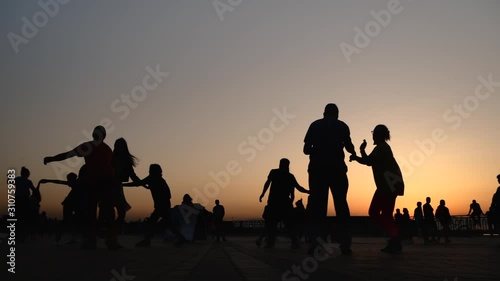 Unrecognizable people silhouettes learning how to dance on city quay at sunset - super slow motion. Warm illumination, evening time. Romantic pairs group dance concept
