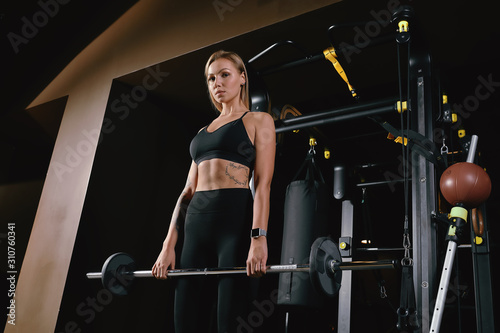 Front view of confident young blonde woman doing weight lifting workout Attractive young woman lifting weight looking forward Strong trained body shape arms chest legs.