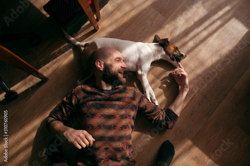 the guy is lying on the floor with the dog and laughing