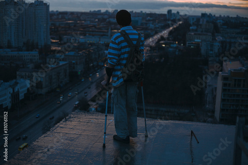 guy without legs crutches on the roof against the backdrop of the night city photo