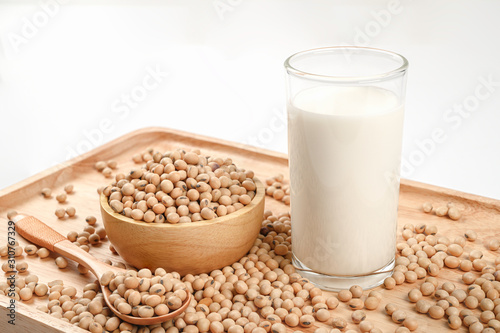 Soy milk in glass with soy beans in wooden bowl and spoon on white background