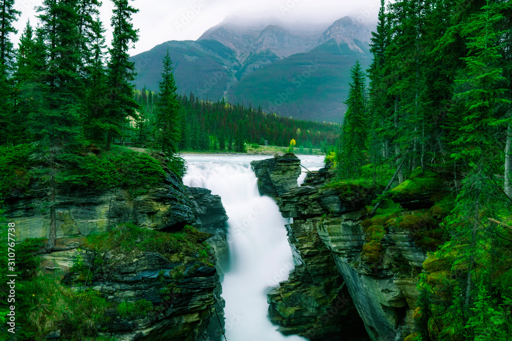Spectacular Waterfall In Beautiful Rocky Mountain Forest.