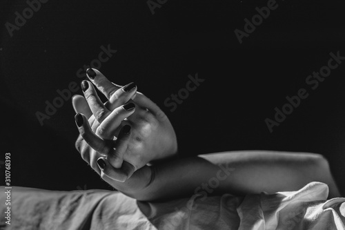 Close up on female young woman's girl's beautiful hands woman lying on the bed black and white nail polish in dark room crossed fingers on sheet gentle passion love temptation emotion concept