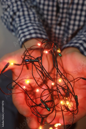 Close up of shining Christmas lights in hands of a man, miracle and winter holidays concept. Beautiful glowing garland in male hands.