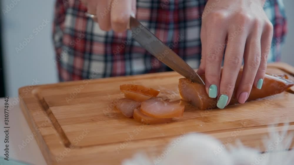 American woman cuts jerky meat standing at table in kitchen interior. Young female cutting jerked filet on wooden board, holding knife in hand. Housewife is preparing delicious dinner at desk in American woman cuts jerky meat standing at table in kitchen interior. Young female cutting jerked filet on wooden board, holding knife in hand. Housewife is preparing delicious dinner at desk in