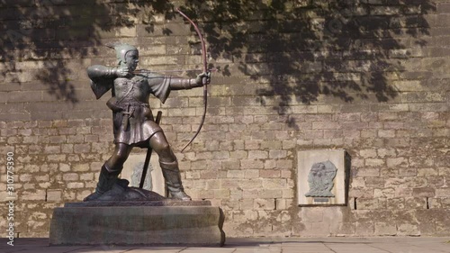 A wide, steady shot of the monument of Robin Hood made of metal located in Nottingham, England, against an aged brick wall. photo