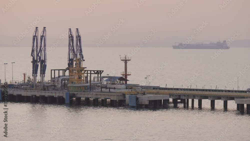 Jetty of iquefied gas terminal with large LNG tanker on horizon of sea in evening Jetty of iquefied gas terminal with large LNG tanker on horizon of sea in evening