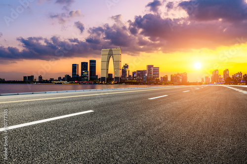 Asphalt road and Suzhou city skyline with beautiful colorful clouds at sunset.