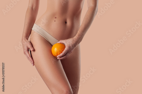 Slim woman is holding orange. Perfect female hips in underwear w