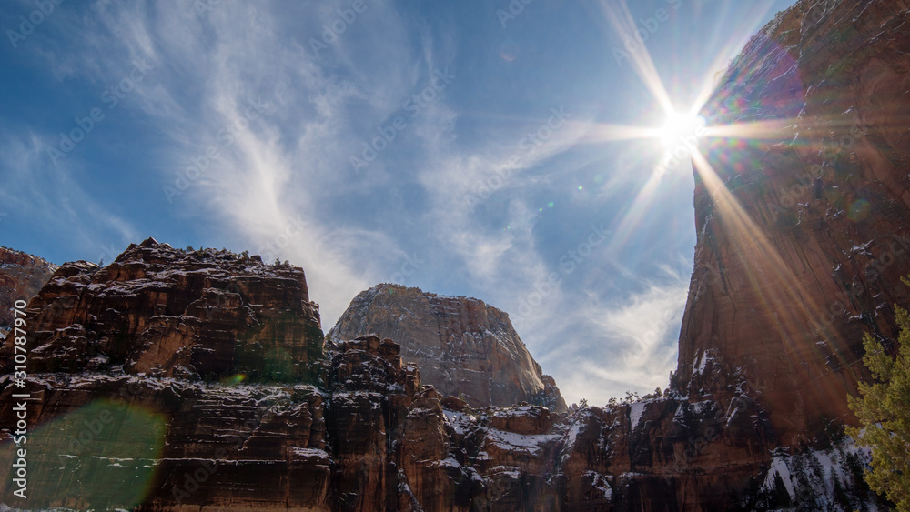 Sun moving behind Angels Landing in Zion viewing the cliffs towering high in the sky.