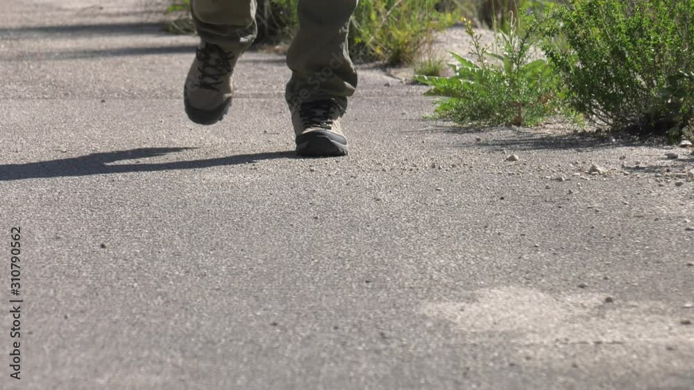 Man in hiking boots walking up track, low angle Man in hiking boots walking up track, low angle