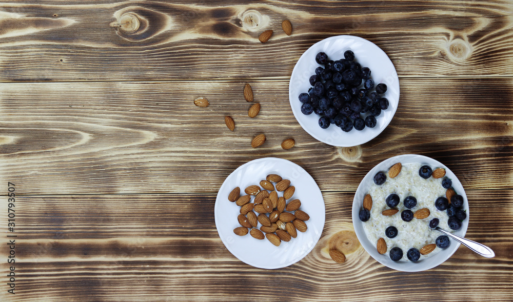 Oatmeal porridge with blueberries and almonds on wooden background