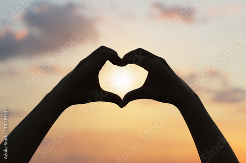 Silhouette of woman hands in heart shape with sunrise.