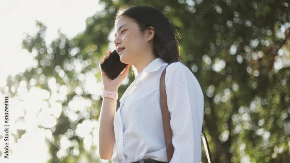 A beautiful asian female office worker in a white shirt is talking on the phone outside the morning at a public park. A beautiful asian female office worker in a white shirt is talking on the phone outside the morning at a public park.