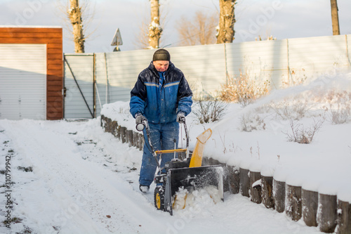 A man cleans snow from sidewalks with snowblower