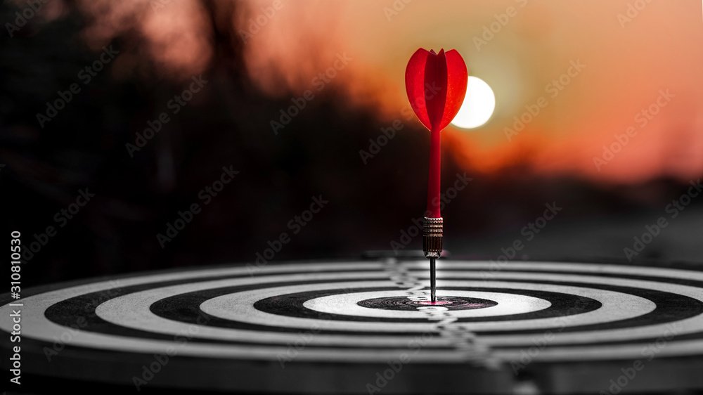 Close up red dart arrow hitting target center dartboard on sunset background. Business targeting and focus concept. Close up red dart arrow hitting target center dartboard on sunset background. Business targeting and focus concept.
