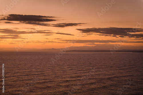 Sunset in Cyprus, Cape Greco. Calm dark sea and orange sky with clouds
