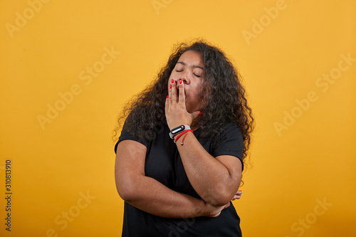 Tired afro-american woman with overweight covered mouth with hands, yawning over isolated orange background wearing fashion black shirt. People lifestyle concepte.