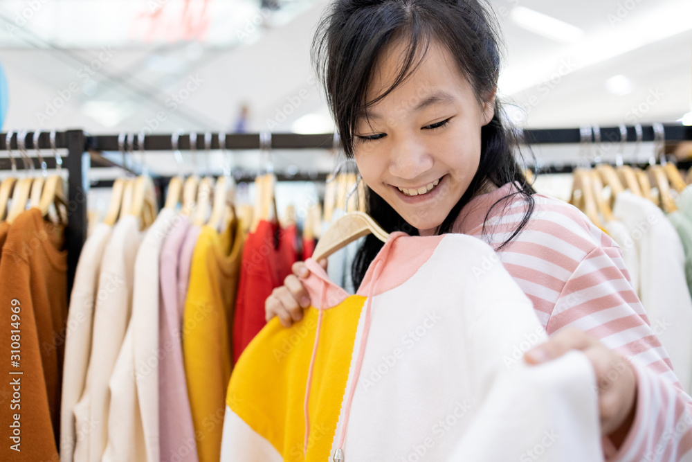 Beautiful asian child girl choosing clothes in shopping center,happy smiling woman customer buying new fashion long sleeved t-shirts during discounted products for herself as a gift in the mall Beautiful asian child girl choosing clothes in shopping center,happy smiling woman customer buying new fashion long sleeved t-shirts during discounted products for herself as a gift in the mall